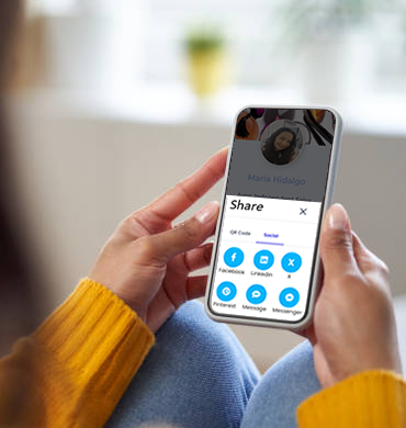 A white woman holding a cellphone in her hands, displaying a uBrand Hub client's digital hub opened to the 'Share' feature. Various social media icons are visible, indicating successful sharing options for the digital business card.